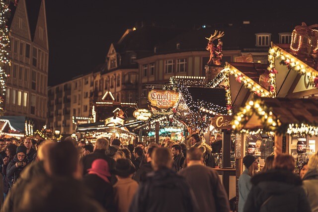 Zahlreiche Menschen von hinten auf einem beleuchteten Weihnachtsmarkt im Dunkeln